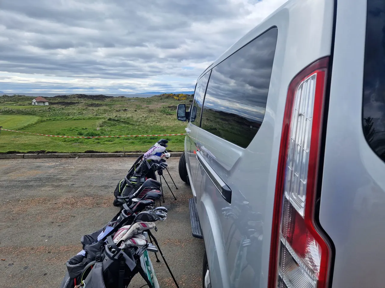 Golf bags beside a B-Direct minibus at a coastal golf course