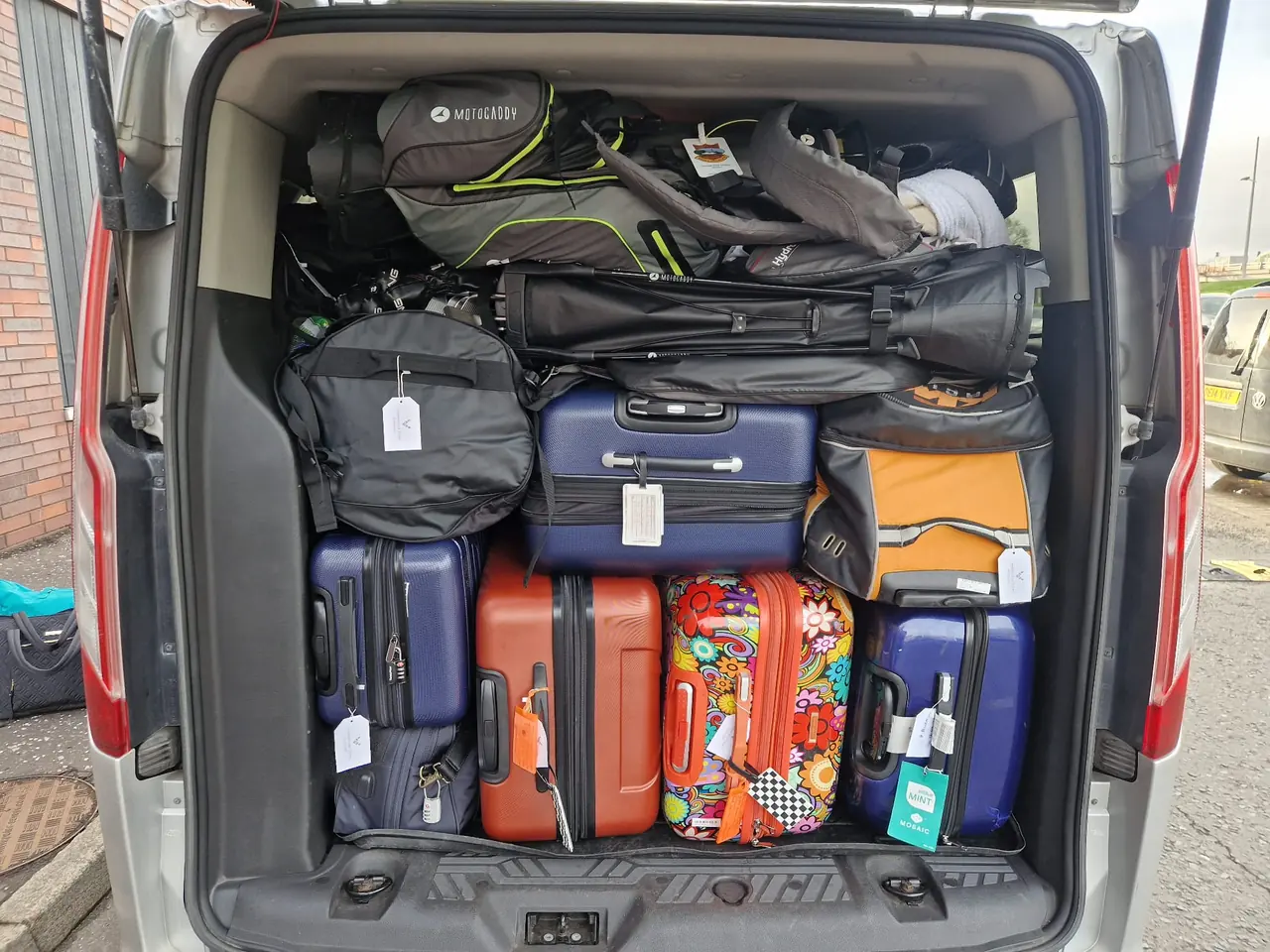 Suitcases and golf travel bags loaded in the back of a B-Direct minibus
